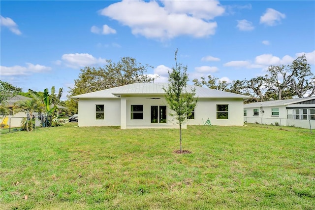 rear view of house with stucco siding, metal roof, a yard, and fence