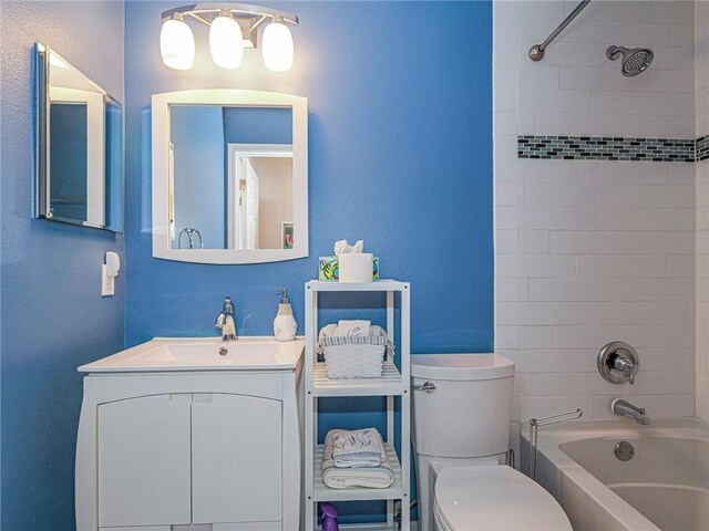 full bathroom featuring tiled shower / bath, vanity, and toilet