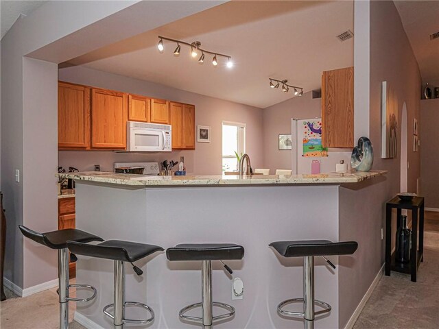 kitchen featuring lofted ceiling, a breakfast bar, light stone countertops, light carpet, and kitchen peninsula