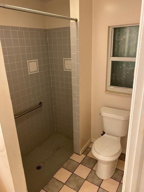 bathroom with tile patterned flooring, tiled shower, and toilet