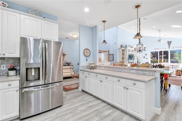 kitchen featuring hanging light fixtures, stainless steel fridge, decorative backsplash, white cabinets, and light wood-type flooring