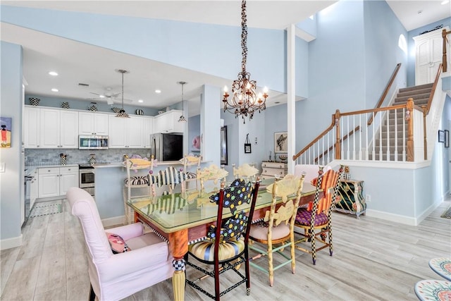 dining area with a high ceiling, ceiling fan with notable chandelier, and light wood-type flooring