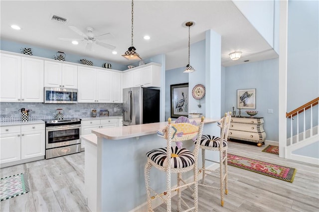 kitchen featuring white cabinetry, pendant lighting, a breakfast bar area, decorative backsplash, and appliances with stainless steel finishes