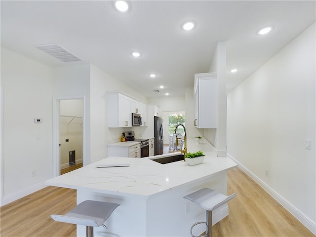 kitchen with kitchen peninsula, a kitchen breakfast bar, stainless steel appliances, sink, and white cabinetry