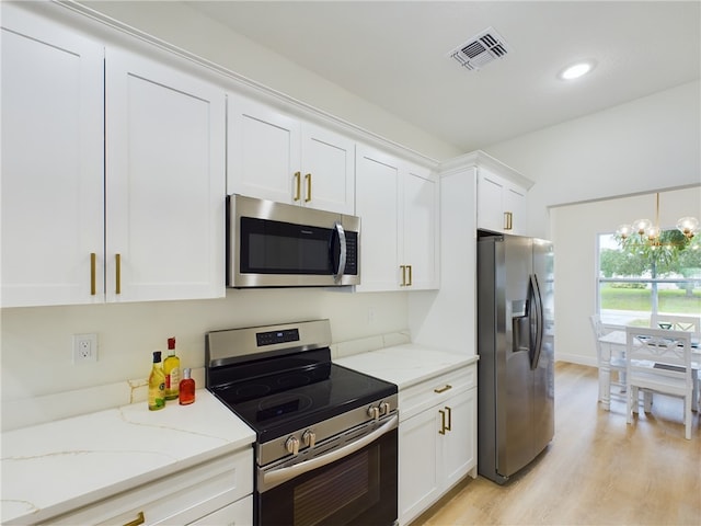 kitchen featuring light stone countertops, light wood-type flooring, stainless steel appliances, a notable chandelier, and white cabinetry