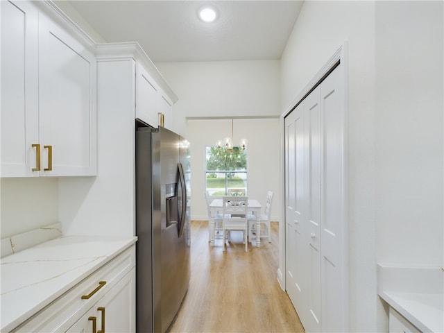 kitchen featuring light stone countertops, stainless steel fridge, decorative light fixtures, light hardwood / wood-style flooring, and white cabinetry