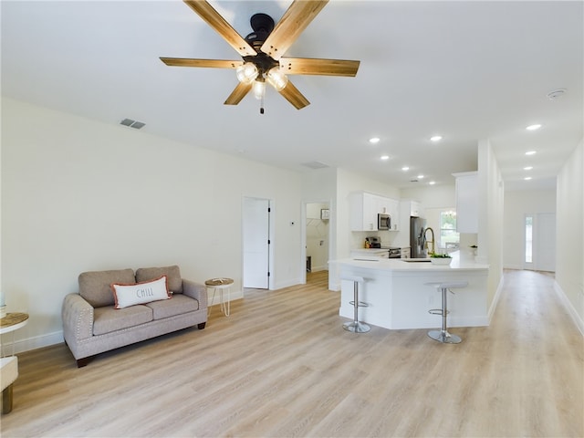 living room with ceiling fan, light wood-type flooring, and sink