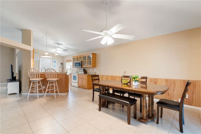 dining room with light tile patterned floors, ceiling fan, lofted ceiling, and wood walls