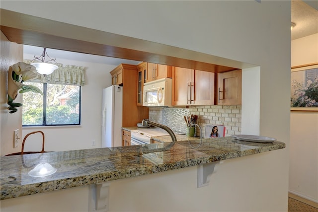 kitchen featuring kitchen peninsula, decorative backsplash, light stone countertops, white appliances, and pendant lighting