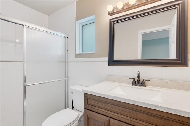 bathroom with tile walls, a shower with door, vanity, and toilet