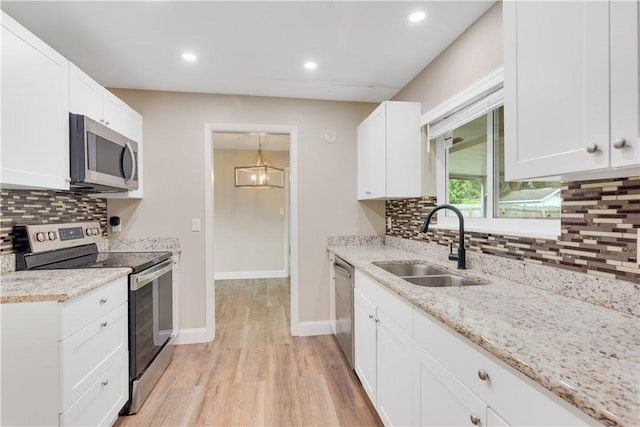 kitchen with sink, white cabinetry, light stone counters, a chandelier, and appliances with stainless steel finishes