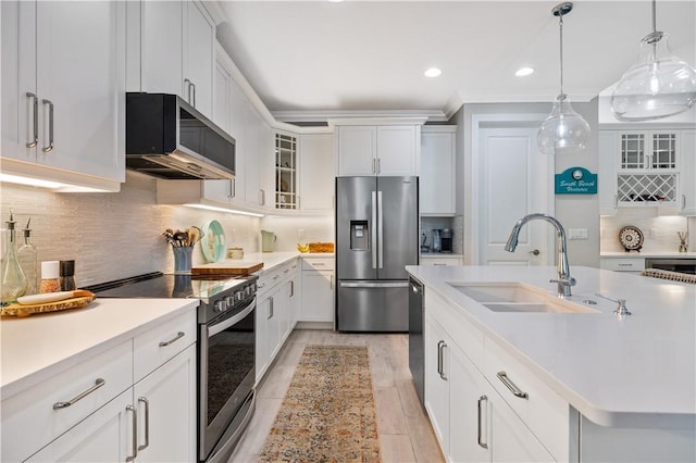 kitchen with tasteful backsplash, glass insert cabinets, light countertops, appliances with stainless steel finishes, and a sink