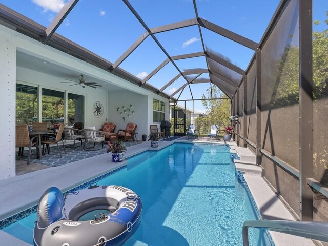 outdoor pool featuring glass enclosure, a ceiling fan, and a patio