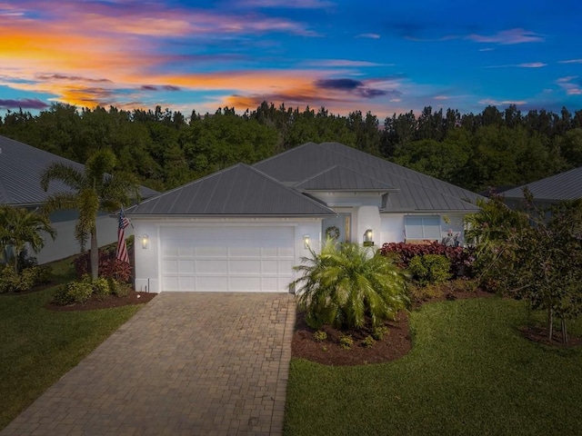 ranch-style home with a front lawn, stucco siding, metal roof, decorative driveway, and an attached garage