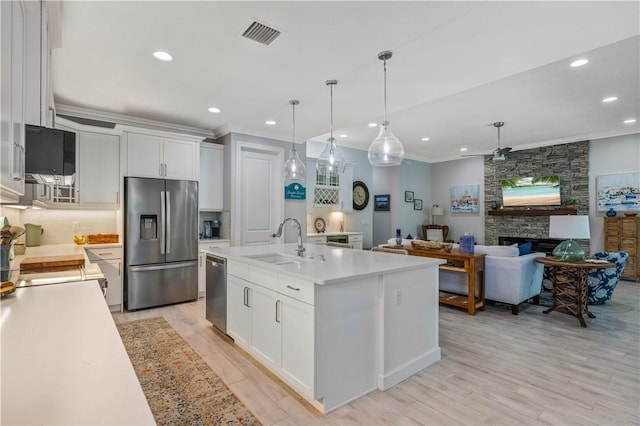 kitchen with a sink, a stone fireplace, ornamental molding, light countertops, and stainless steel appliances