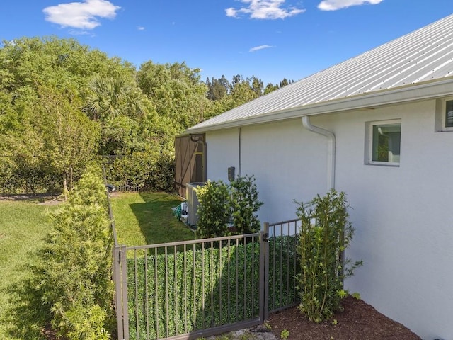 view of side of home with fence, stucco siding, central air condition unit, a lawn, and metal roof