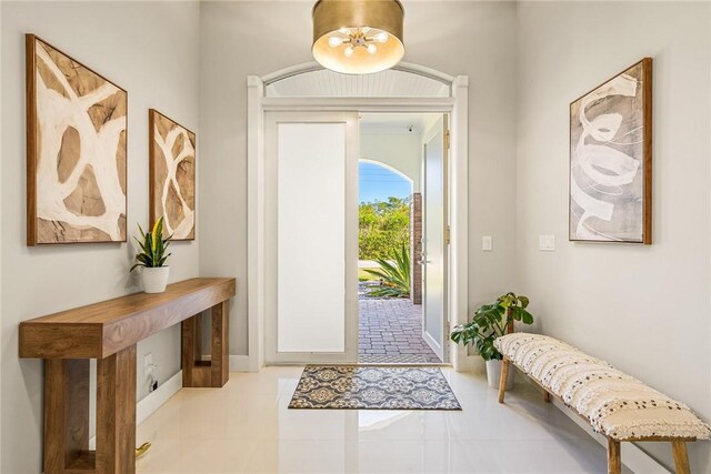 tiled entryway with a chandelier and baseboards