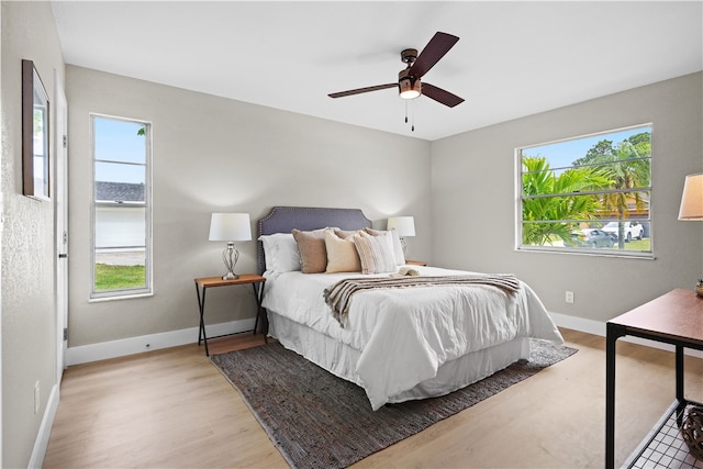 bedroom with light wood-type flooring, ceiling fan, multiple windows, and baseboards