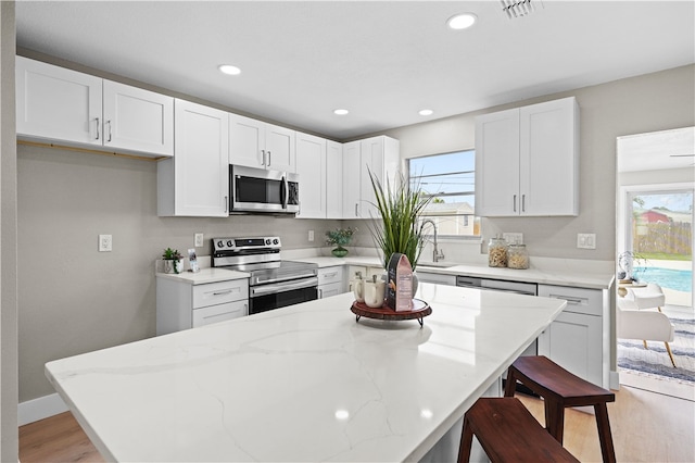 kitchen featuring white cabinets, appliances with stainless steel finishes, a breakfast bar, and a healthy amount of sunlight