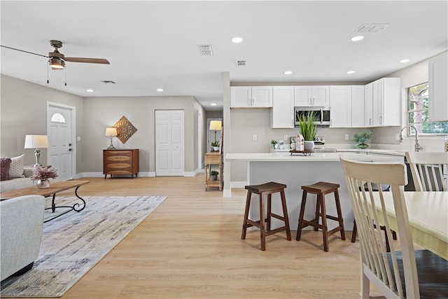 kitchen featuring visible vents, light wood-style flooring, stainless steel microwave, a breakfast bar, and recessed lighting