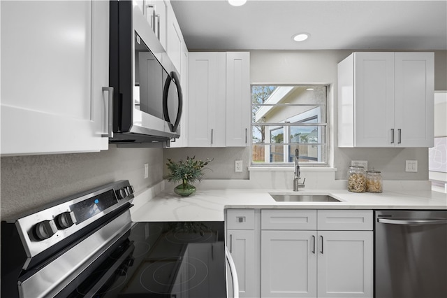 kitchen with appliances with stainless steel finishes, white cabinets, a sink, and light stone counters