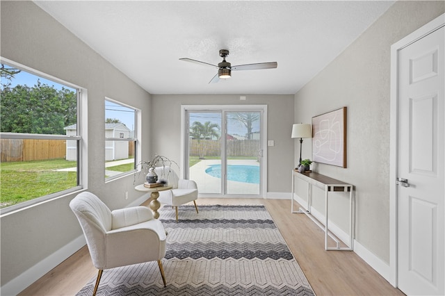 living area featuring a ceiling fan, light wood-style flooring, and baseboards