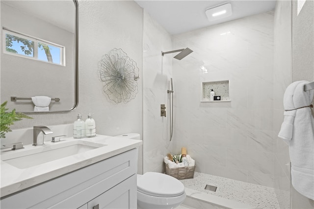 bathroom with a tile shower, vanity, and toilet