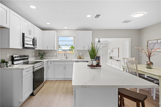 kitchen with light wood-style flooring, a sink, visible vents, appliances with stainless steel finishes, and a center island