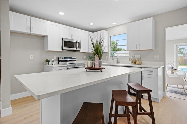 kitchen featuring appliances with stainless steel finishes, a healthy amount of sunlight, white cabinetry, and a breakfast bar area