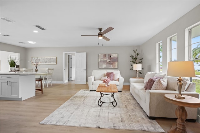 living area with light wood-style flooring, a ceiling fan, visible vents, and baseboards