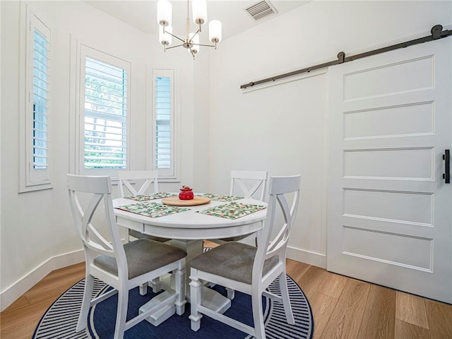 dining area featuring light wood-type flooring, a barn door, and a notable chandelier