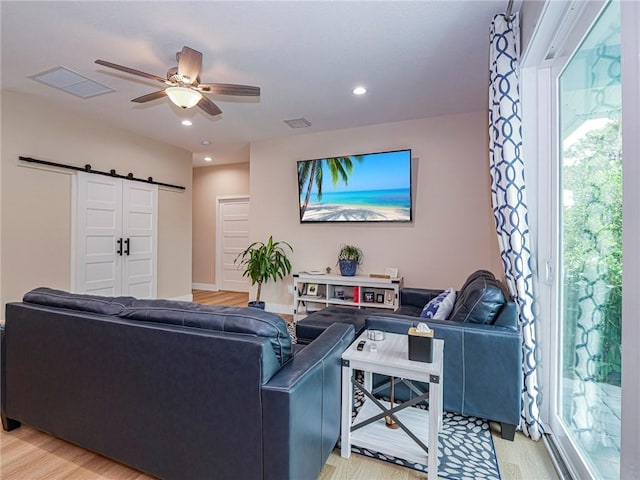 living room featuring a barn door, light hardwood / wood-style floors, a wealth of natural light, and ceiling fan