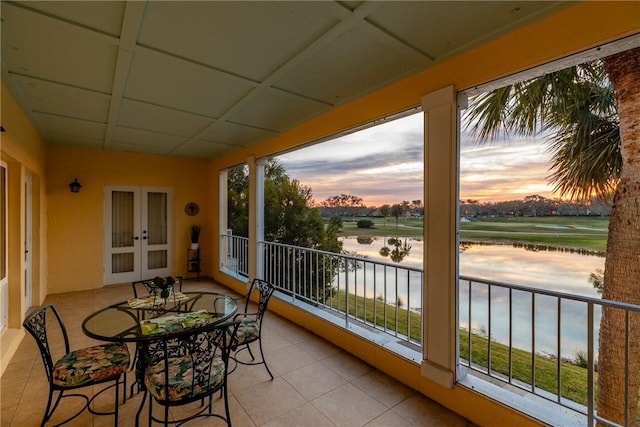 balcony at dusk featuring a water view and french doors