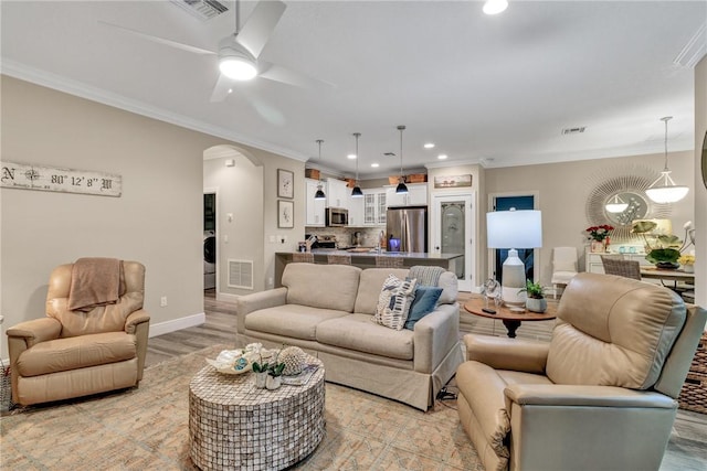 living room with washer / dryer, light hardwood / wood-style flooring, ceiling fan, and crown molding