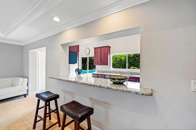 kitchen with kitchen peninsula, sink, ornamental molding, a breakfast bar, and light stone countertops