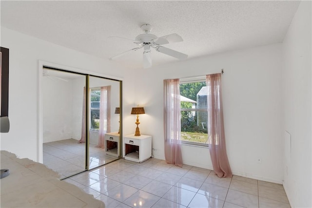 unfurnished bedroom featuring a textured ceiling, a closet, a ceiling fan, light tile patterned flooring, and baseboards