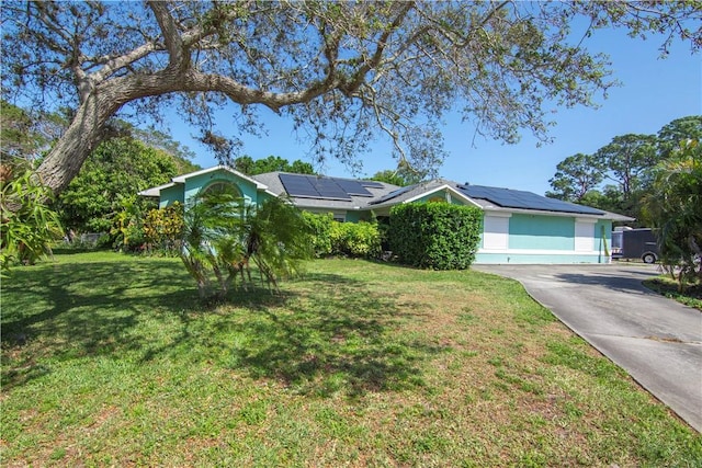 view of front of property with concrete driveway, a front lawn, and roof mounted solar panels