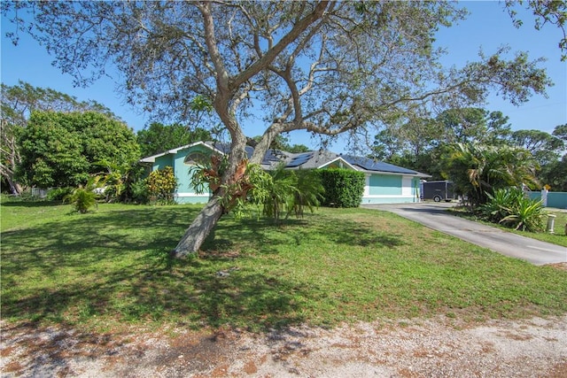 view of front facade with a front yard, driveway, fence, and roof mounted solar panels
