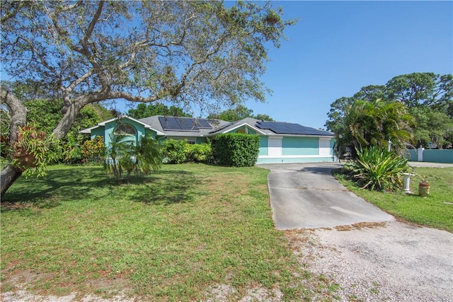 single story home featuring roof mounted solar panels, driveway, and a front yard