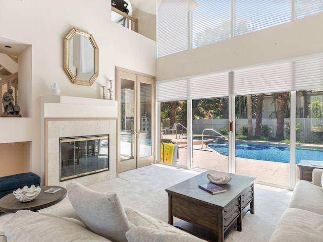 living room featuring light carpet, french doors, a towering ceiling, and a tile fireplace