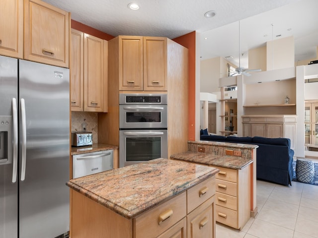 kitchen featuring ceiling fan, light stone counters, light brown cabinetry, a kitchen island, and appliances with stainless steel finishes