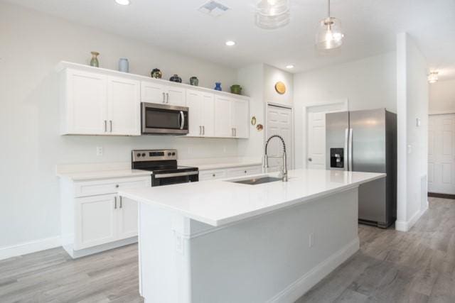 8286 96th Ct, Vero Beach, FL 32967 - kitchen with appliances with stainless steel finishes, a sink, a kitchen island with sink, light wood finished floors, and white cabinets
