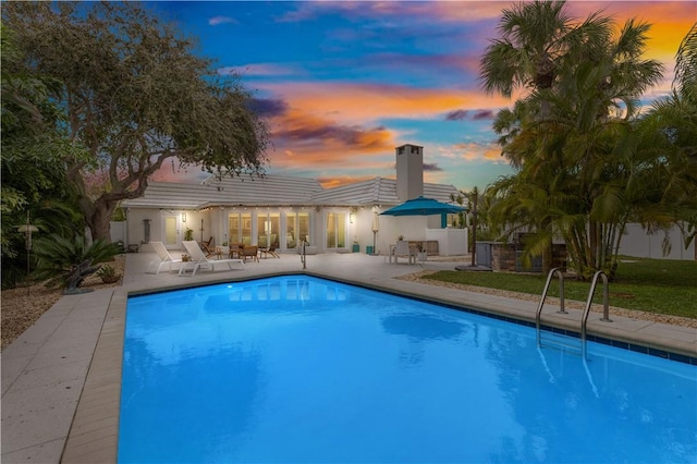 pool at dusk with an outdoor pool and a patio area