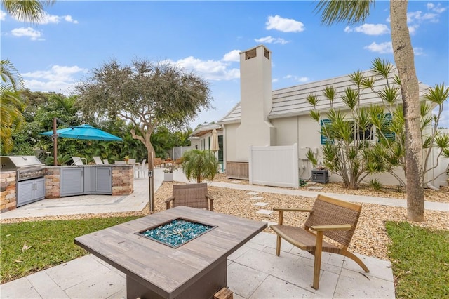 view of patio featuring an outdoor kitchen, area for grilling, central AC unit, fence, and an outdoor fire pit