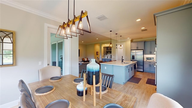 dining space with sink, light wood-type flooring, and ornamental molding