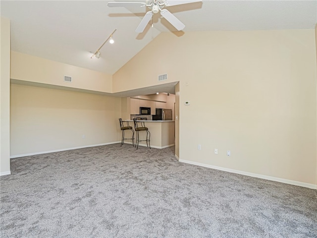 unfurnished living room with carpet floors, ceiling fan, rail lighting, and high vaulted ceiling