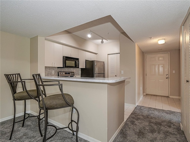 kitchen featuring white cabinets, a kitchen breakfast bar, a textured ceiling, appliances with stainless steel finishes, and kitchen peninsula