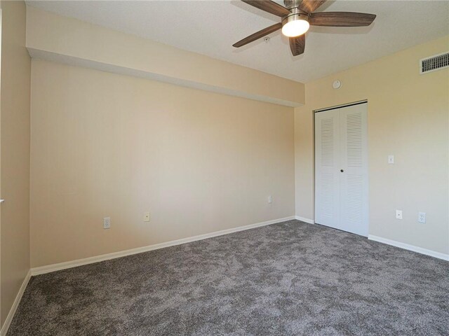 unfurnished bedroom with ceiling fan, a closet, and dark colored carpet