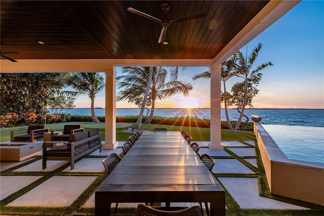 patio terrace at dusk with ceiling fan, an outdoor living space, and a water view