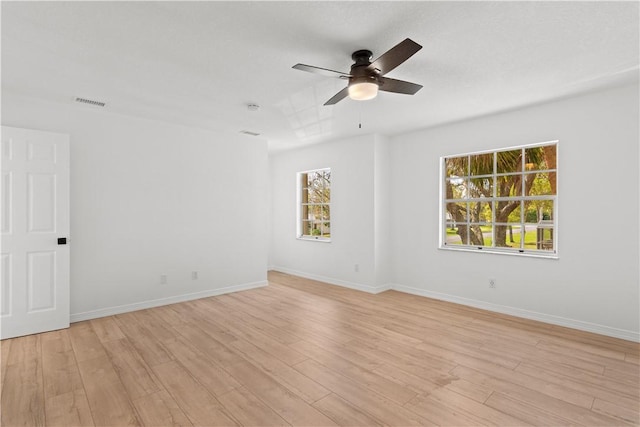 spare room featuring light wood-type flooring, visible vents, ceiling fan, and baseboards